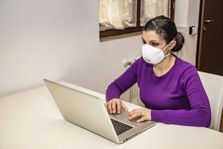 Corona Virus, Covid-19. Stay at home. Quarantine. Protection mask. A beautiful Caucasian woman forced to stay home to prevent virus infection, works on the laptop. Smart Working.の写真素材