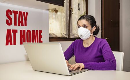 Corona Virus, Covid-19. Stay at home. Quarantine. Protection mask. A beautiful Caucasian woman forced to stay home to prevent virus infection, works on the laptop. Smart Working.の写真素材