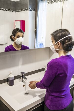 Corona Virus, Covid-19. Stay at home. Quarantine. Protection mask. A beautiful Caucasian woman washes her hands to prevent virus infection in the bathroom in front of the mirror.の写真素材