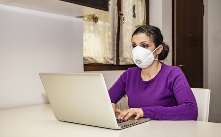 Corona Virus, Covid-19. Stay at home. Quarantine. Protection mask. A beautiful Caucasian woman forced to stay home to prevent virus infection, works on the laptop. Smart Working.の写真素材