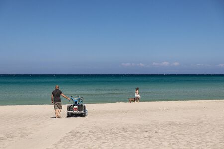 The bay of Torre dell'Orso, with its high cliffs, in Salento, Puglia, Italy. Turquoise sea and blue sky, sunny day in summer. In a bathhouse, a man cleans the sand with a small tractor (sand cleaner).の写真素材