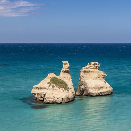The bay of Torre dell'Orso, with its high cliffs, in Salento, Puglia, Italy. Turquoise sea and blue sky, sunny day in summer. The stacks called the Two Sisters. A person swims in the clear waterの写真素材