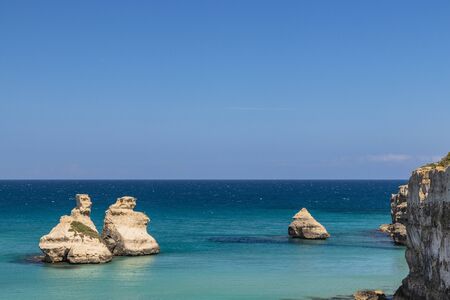 The bay of Torre dell'Orso, with its high cliffs, in Salento, Puglia, Italy. Turquoise sea and blue sky, sunny day in summer. The stacks called the Two Sisters, immersed in the sea.の写真素材