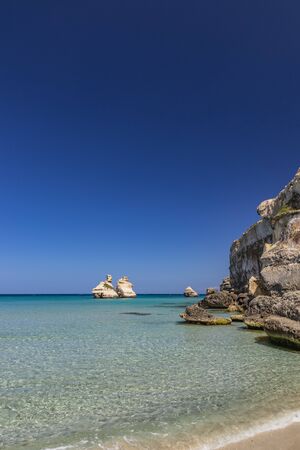 The bay of Torre dell'Orso, with its high cliffs, in Salento, Puglia, Italy. Turquoise sea and blue sky, sunny day in summer. A beach of fine white and pink sand. The stacks called the Two Sisters.の写真素材