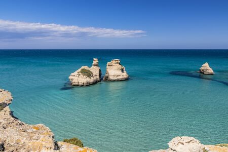 The bay of Torre dell'Orso, with its high cliffs, in Salento, Puglia, Italy. Turquoise sea and blue sky, sunny day in summer. The stacks called the Two Sisters, immersed in the sea.の写真素材