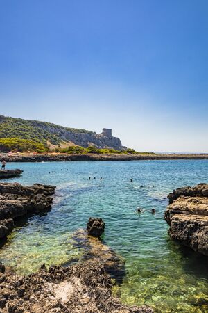 The wonderful bay of Porto Selvaggio, with pebbly and rocky beach. In NardÃ², Italy, Puglia, Salento. People sunbathe and swim in the turquoise sea. The Torre dell'Alto on the promontory. Wild nature.の写真素材