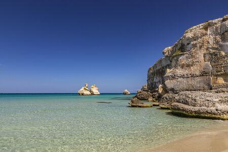 The bay of Torre dell'Orso, with its high cliffs, in Salento, Puglia, Italy. Turquoise sea and blue sky, sunny day in summer. A beach of fine white and pink sand. The stacks called the Two Sisters.の写真素材