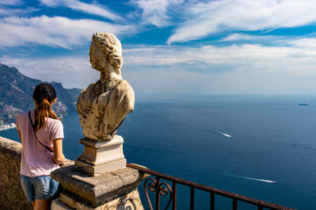 October 14, 2018 - Ravello, Campania, Italy - A girl admires the spectacular view from the Terrace of the Infinity, in Villa Cimbrone, on the Amalfi coast. The blue sky and some marble busts.のeditorial素材