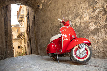 June 30, 2019 - Rome, Lazio, Italy - A red Piaggio Vespa Sprint, parked in an alleyway of an ancient village, in Italy. The scooter symbol of Italian design.のeditorial素材