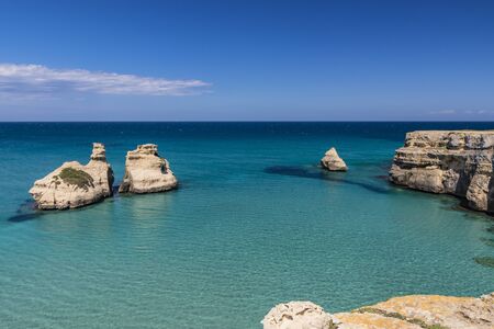 The bay of Torre dell'Orso, with its high cliffs, in Salento, Puglia, Italy. Turquoise sea and blue sky, sunny day in summer. The stacks called the Two Sisters, immersed in the sea.の写真素材