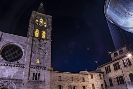The Romanesque Church of San Michele in the medieval village of Bevagna. Umbria, Italy. The travertine facade, with the large rose window and the Gothic bell tower. The marble fountain. Night viewの写真素材