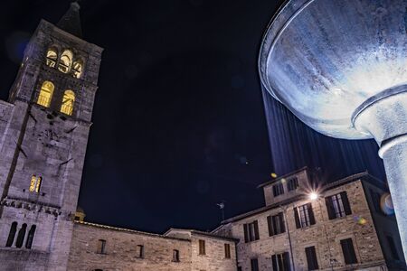 The Romanesque Church of San Michele in the medieval village of Bevagna. Umbria, Italy. The travertine facade, with the large rose window and the Gothic bell tower. The marble fountain. Night viewの写真素材