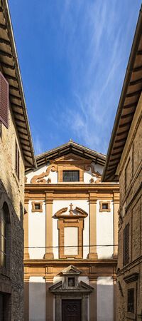 One of the ancient churches of the medieval village of Bevagna. Perugia, Umbria, Italy. The facade of the church can be seen between the buildings. The blue sky.の写真素材