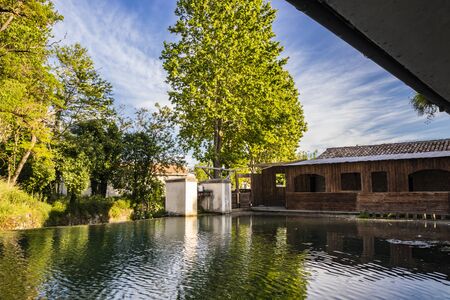 The ancient wooden wash house, on the river, in the medieval village of Bevagna. Perugia, Umbria, Italy. The blue sky at sunset. Trees and vegetation reflected on the water surface.の写真素材