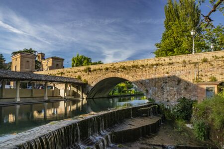 The ancient wash-house and the masonry bridge over the river, in the medieval village of Bevagna. Perugia, Umbria, Italy. Blue sky at sunset. Trees and vegetation. The reflection on the water surface.の写真素材