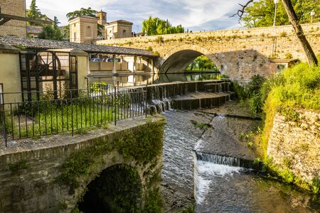 The ancient wash-house and the masonry bridge over the river, in the medieval village of Bevagna. Perugia, Umbria, Italy. Blue sky at sunset. Trees and vegetation. The reflection on the water surface.の写真素材