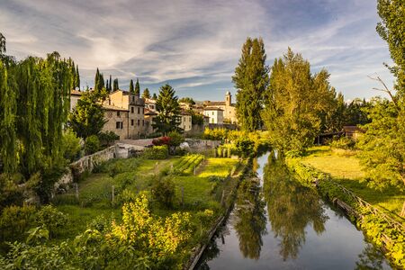 The Chiasco river that crosses the ancient medieval village of Bevagna. Perugia, Umbria, Italy. Trees, vegetation, cultivated gardens. The blue sky at sunset, in the summer.の写真素材