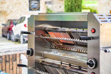 A man cooks the Arrosticini, skewers of sheep meat, a typical dish of Abruzzo cuisine, on a gas grill, in a stall of a village festival. Grilled meat, barbeque. Street food.の写真素材