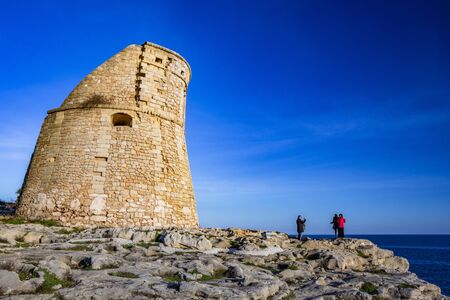 The ancient watch tower of Porto Miggiano, built on the cliffs overlooking the sea. Some people do photo and selfie with the sea in the background. Santa Cesarea Terme, Puglia, Salento, Italy.の写真素材