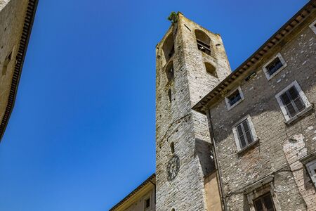 The Palazzo del PodestÃ , in Piazza dei Priori in the ancient medieval village of Narni. The stone bell tower and the clock. Umbria, Terni, Italy. The blue sky on a summer day.の写真素材