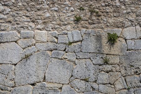 The ancient megalithic walls surround the acropolis of Amelia, in Umbria, Italy. Texture composed ofirregular huge blocks of stone. The grass grows between the interstices of the wall.の写真素材