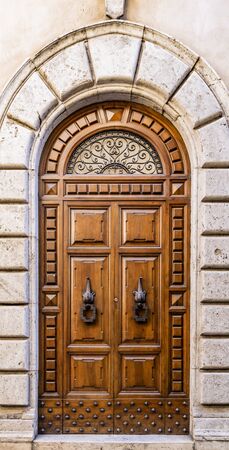 An ancient wooden portal with iron knocker, arch and window with metal decorations. Stone and marble frame. Italian craftsmanship. In an Italian city.の写真素材