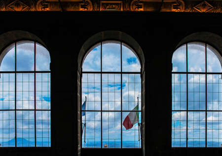 June 3, 2016 - Caprarola, Viterbo, Lazio, Italy - Villa Farnese. Three large arched windows, overlooking the city, the Italian flag, the mountains at the bottom, the cloudy blue sky. In backlight.のeditorial素材