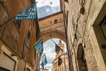 June 1, 2019 - Foligno, Perugia, Umbria, Italy - An alley in the center of Foligno, with blue, black and yellow flags of the districts. At the bottom, under the arch, the Town Hall of the city.の写真素材