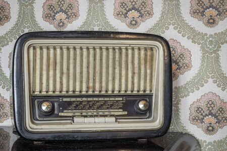 An old transistor radio, with knobs and buttons for manual tuning. In the background a vintage wallpaper. Ancient object, worn and ruined by time.の写真素材