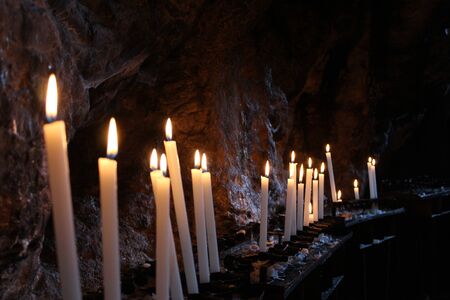 Row of lit candles on offer to the cult of the Virgin Mary (Madonna), in the cave of the sanctuary of the Mentorella, in Guadagnolo. Rome, Lazio, Italy. Sacred place of prayer, peace and silence.の写真素材