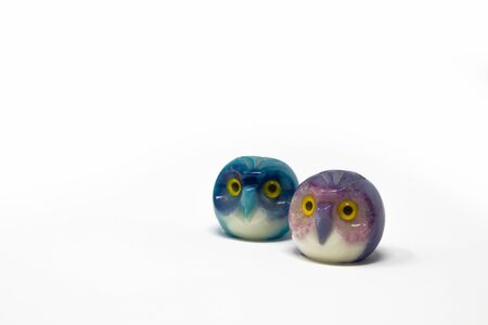 Lucky owl ornament. Small glass lucky object, charm. Blu, azzurro, lilla, viola, giallo. Isolated on white background. Tradition has it that a pair (couple) of owls bring luck. の写真素材