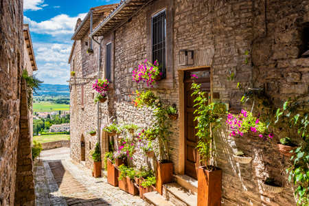 A characteristic alley of the medieval village, with stone and brick houses, plants and flowers on the windows. In Spello, province of Perugia, Umbria, Italy.の写真素材