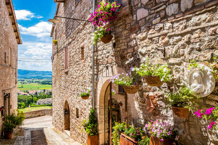 A characteristic alley of the medieval village, with stone and brick houses, plants and flowers on the windows. In Spello, province of Perugia, Umbria, Italy.の写真素材