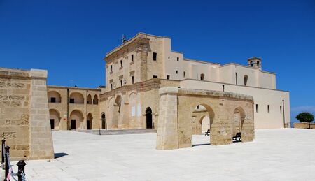 The Basilica of Santa Maria de finibus terrae in the town of Santa Maria di Leuca, in Salento, Puglia, Lecce, Italy. The blue sky and lighthouse. The statue of the Madonna on top of a column, obelisk.の写真素材