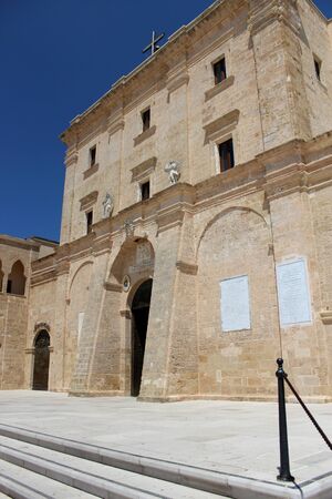 The Basilica of Santa Maria de finibus terrae in the town of Santa Maria di Leuca, in Salento, Puglia, Lecce, Italy. The blue sky and lighthouse. The statue of the Madonna on top of a column, obelisk.の写真素材