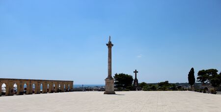 The Basilica of Santa Maria de finibus terrae in the town of Santa Maria di Leuca, in Salento, Puglia, Lecce, Italy. The blue sky and lighthouse. The statue of the Madonna on top of a column, obelisk.の写真素材