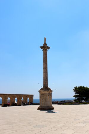 The Basilica of Santa Maria de finibus terrae in the town of Santa Maria di Leuca, in Salento, Puglia, Lecce, Italy. The blue sky and lighthouse. The statue of the Madonna on top of a column, obelisk.の写真素材