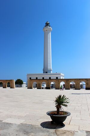 The Basilica of Santa Maria de finibus terrae in the town of Santa Maria di Leuca, in Salento, Puglia, Lecce, Italy. The blue sky and lighthouse. The statue of the Madonna on top of a column, obelisk.の写真素材
