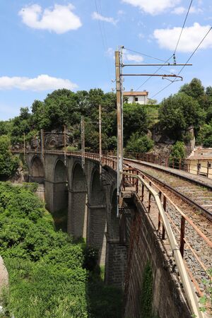 The railroad tracks pass over a stone bridge through a landscape full of vegetation and trees. Elevated rail in perspective. Stone arches.の写真素材