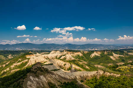 Civita di Bagnoregio, Viterbo, Tuscia, Lazio, Italy. A view of the valley of the badlands, formed by landslides and by the erosion of the tufa, lava and clayey rock. Blue sky and green mountains.の写真素材