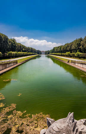 July 3, 2020 - Royal Palace of (Reggia di) Caserta - The very long basin of the park's artificial lake. The perspective view. The marble statues look and extend their hand towards the palace. Blue skyのeditorial素材