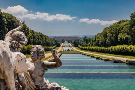 July 3, 2020 - Royal Palace of (Reggia di) Caserta - The very long basin of the park's artificial lake. The perspective view. The marble statues look and extend their hand towards the palace. Blue skyのeditorial素材