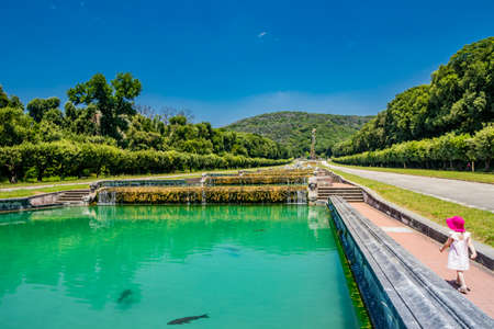 July 3, 2020 - Royal Palace of (Reggia di) Caserta - The very long basin of the park's artificial lake. The perspective view. The marble statues look and extend their hand towards the palace. Blue skyのeditorial素材