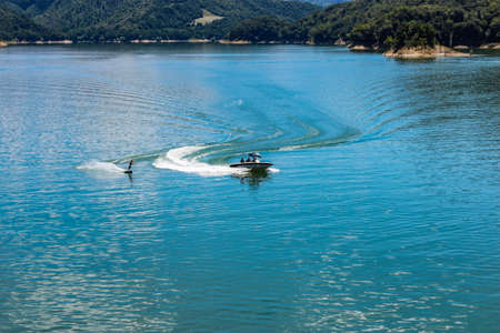 The lake of Salto, the largest artificial lake in Lazio, in the province of Rieti and created by damming the Salto river with the Salto dam. A sportsman practices water skiing towed by a motorboat.の写真素材