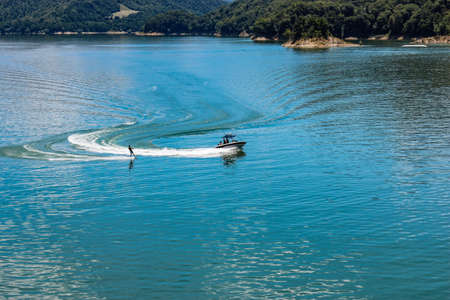 The lake of Salto, the largest artificial lake in Lazio, in the province of Rieti and created by damming the Salto river with the Salto dam. A sportsman practices water skiing towed by a motorboat.の写真素材