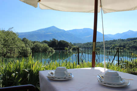 The tables of a hotel for breakfast by the lake. View of the Scandarello lake, in Amatrice, in the province of Rieti, in Lazio, Italy. The blue sky in summer. the green mountains in the background.のeditorial素材