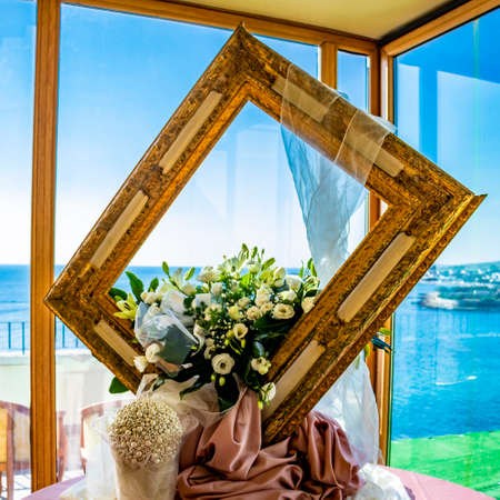 Floral decorations for wedding, in an Italian restaurant, composed of a large wooden frame. The beautiful view of the sea from the large window.の写真素材