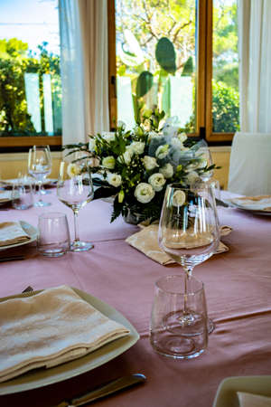 Table set for a ceremony in an Italian restaurant. Celebrations for a wedding. Basket with Champagne. Floral decorations. Pink tablecloth. Luxury, elegance, refinement.の写真素材