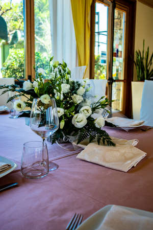 Table set for a ceremony in an Italian restaurant. Celebrations for a wedding. Basket with Champagne. Floral decorations. Pink tablecloth. Luxury, elegance, refinement.の写真素材
