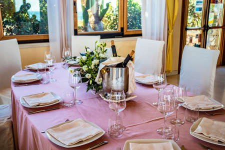 Table set for a ceremony in an Italian restaurant. Celebrations for a wedding. Basket with Champagne. Floral decorations. Pink tablecloth. Luxury, elegance, refinement.の写真素材